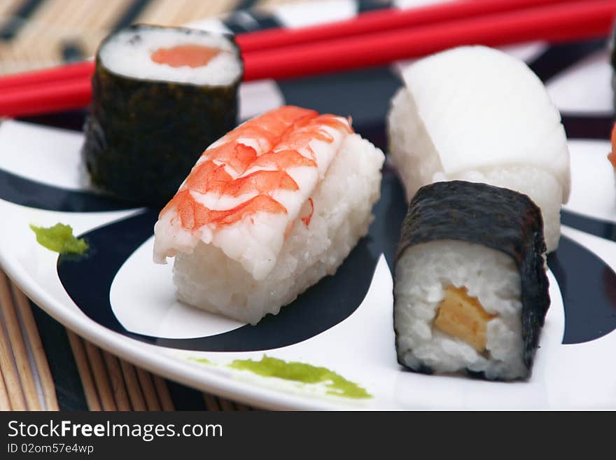 Assortment of sushi on a plate with red chopsticks on a circular decorated plate, on a wood table-cloth, close-up. Assortment of sushi on a plate with red chopsticks on a circular decorated plate, on a wood table-cloth, close-up