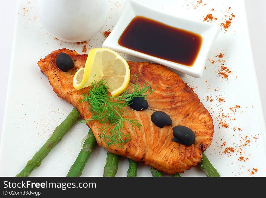 Salmon fried with spices with a lemon on a white plate with fennel