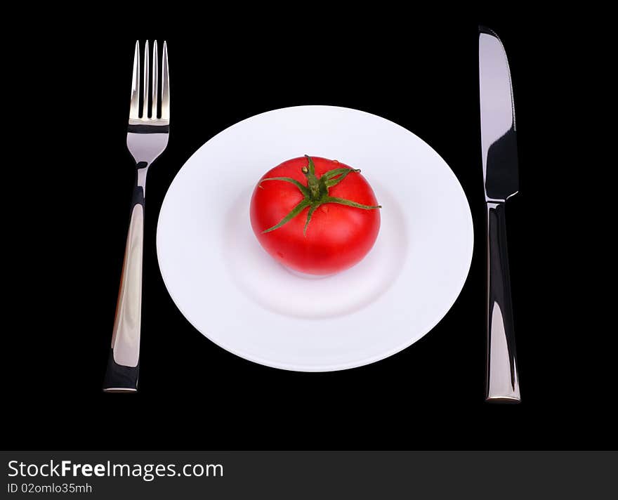 The knife, fork and fresh tomato on white plate. Black background. Isolated object