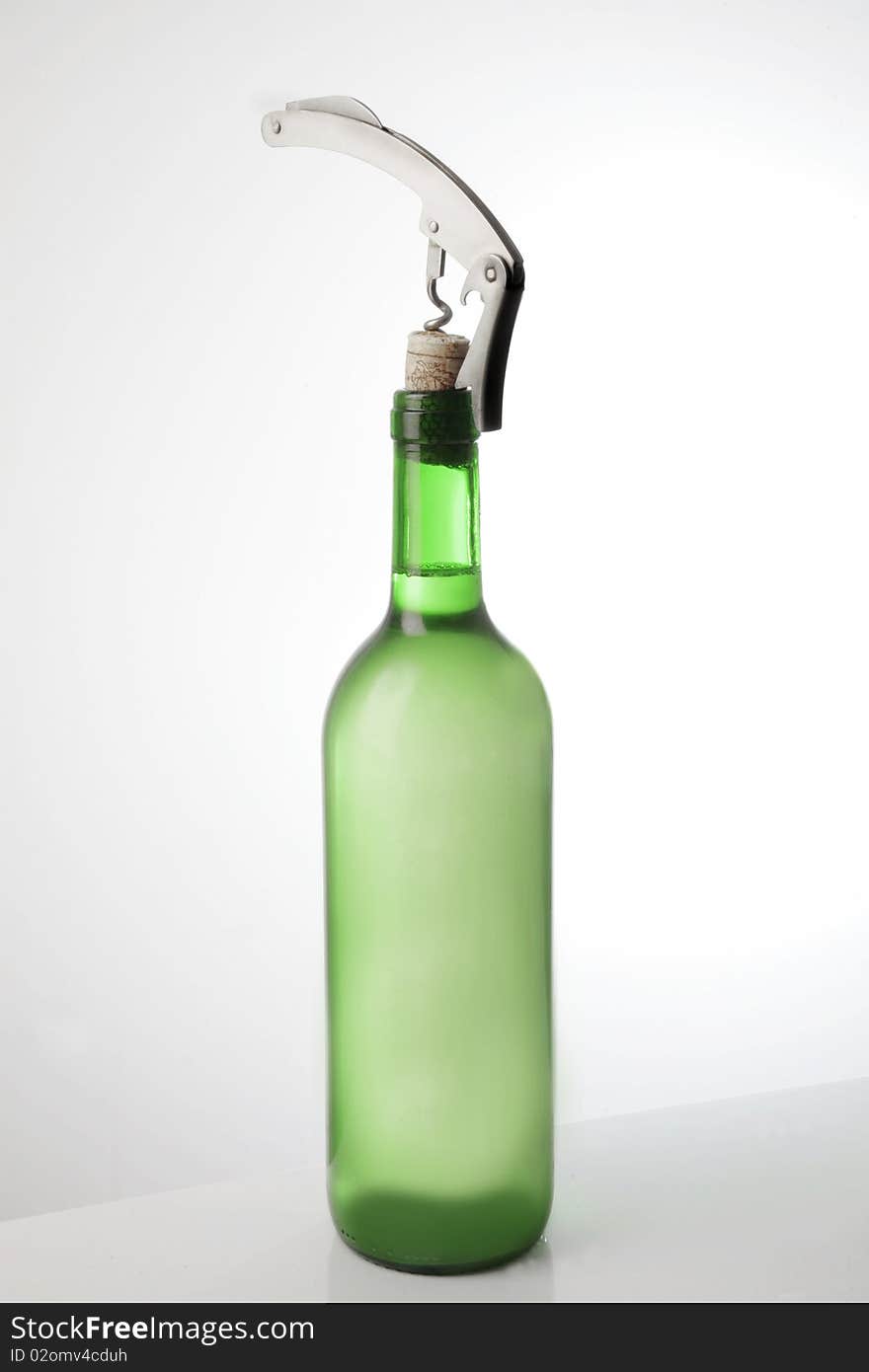 A white wine bottle with a corkscrew in its cork. A white wine bottle with a corkscrew in its cork