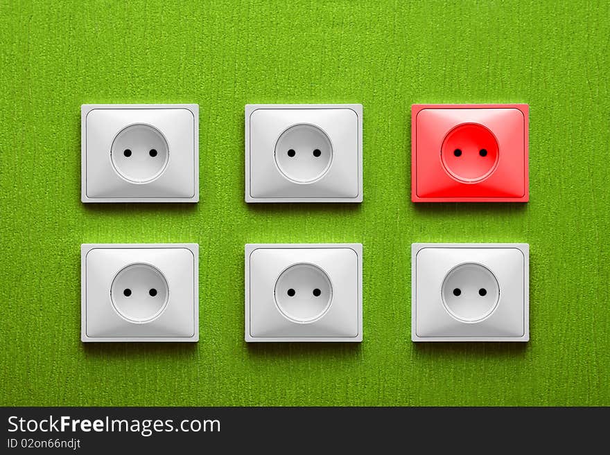 Five white and one red electric sockets in a green wall. Five white and one red electric sockets in a green wall