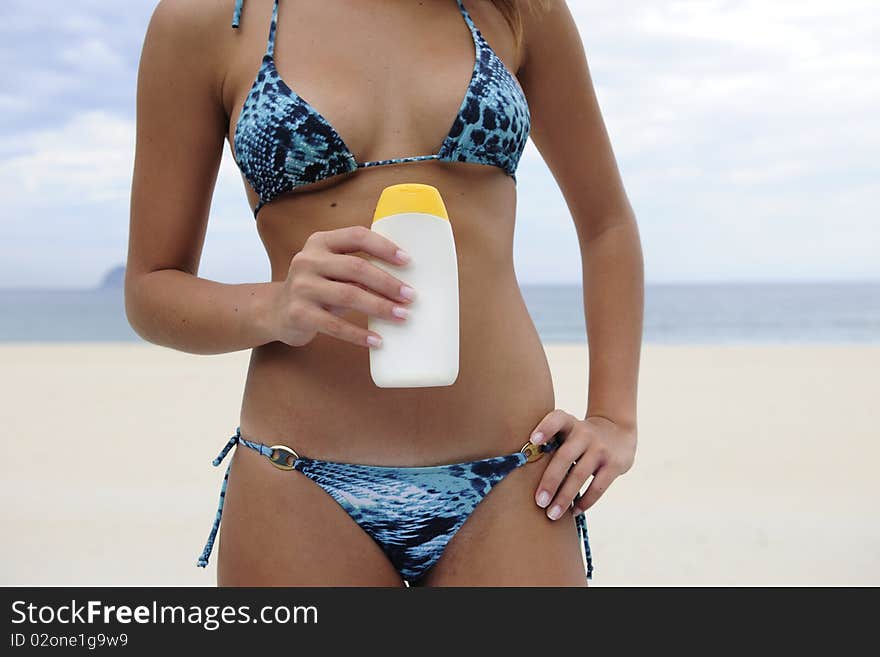 Sexy woman in bikini holding suncream at the beach