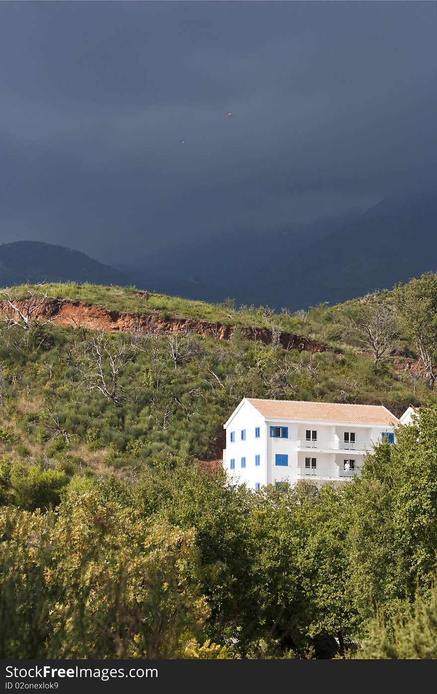 View of alone white building on the hillside at the foot of the mountains on the background of stormy skies near the town of Budva, Montenegro. View of alone white building on the hillside at the foot of the mountains on the background of stormy skies near the town of Budva, Montenegro