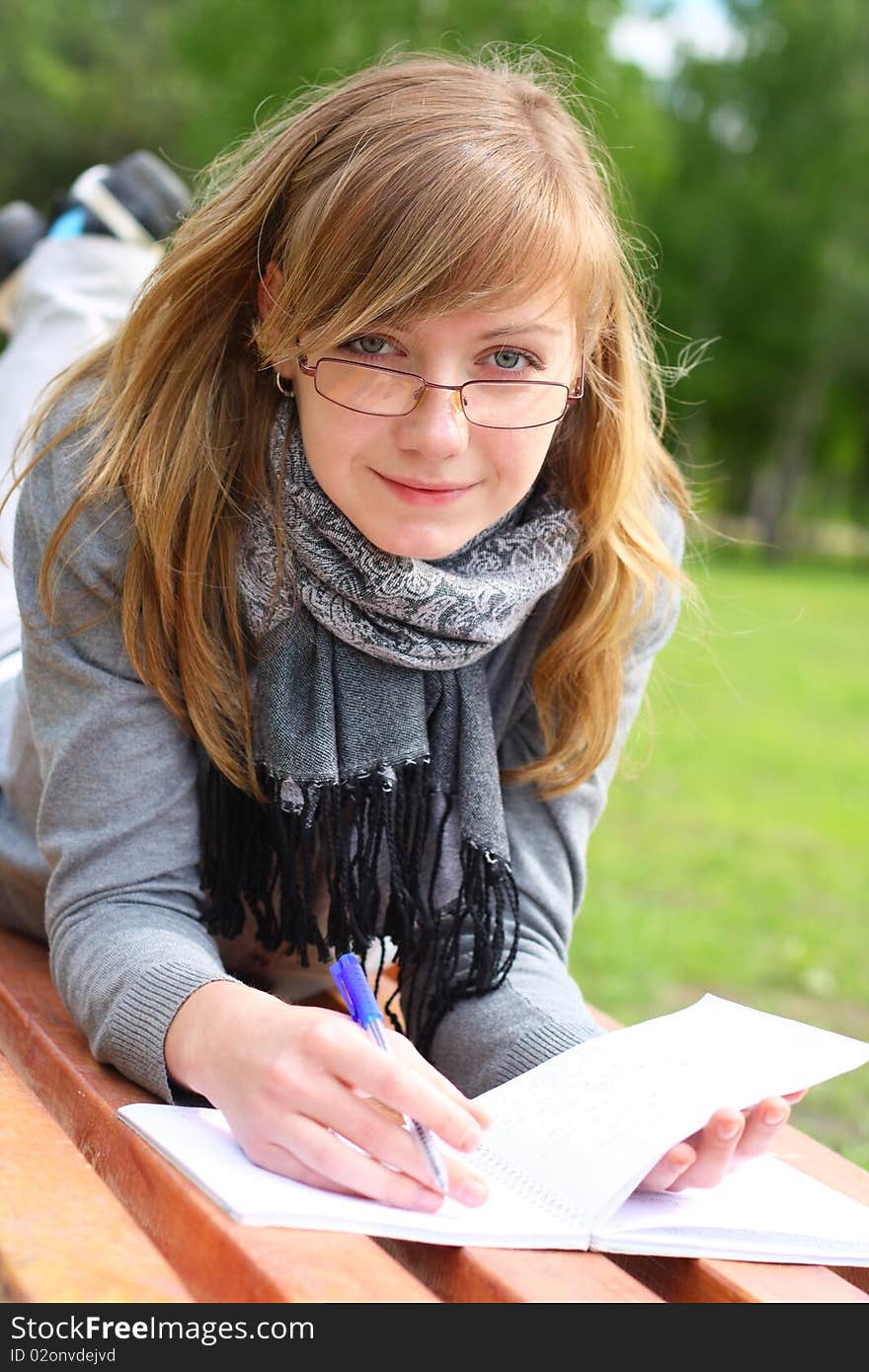 The girl lay on a bench, and writes. Outdoors