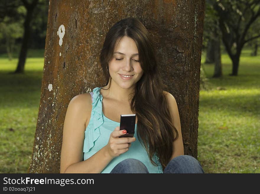 Young woman making a sms in green park. Young woman making a sms in green park