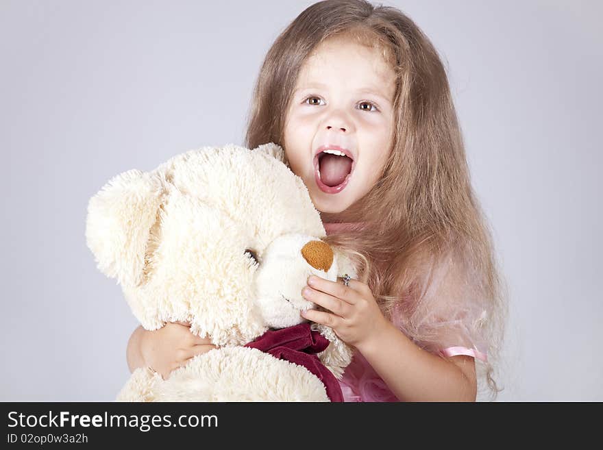 Little shouting girl embraces bear cub. Studio shot.