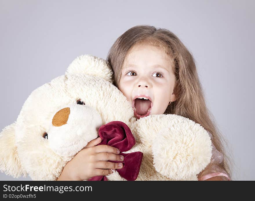 Little shouting girl embraces bear cub. Studio shot.