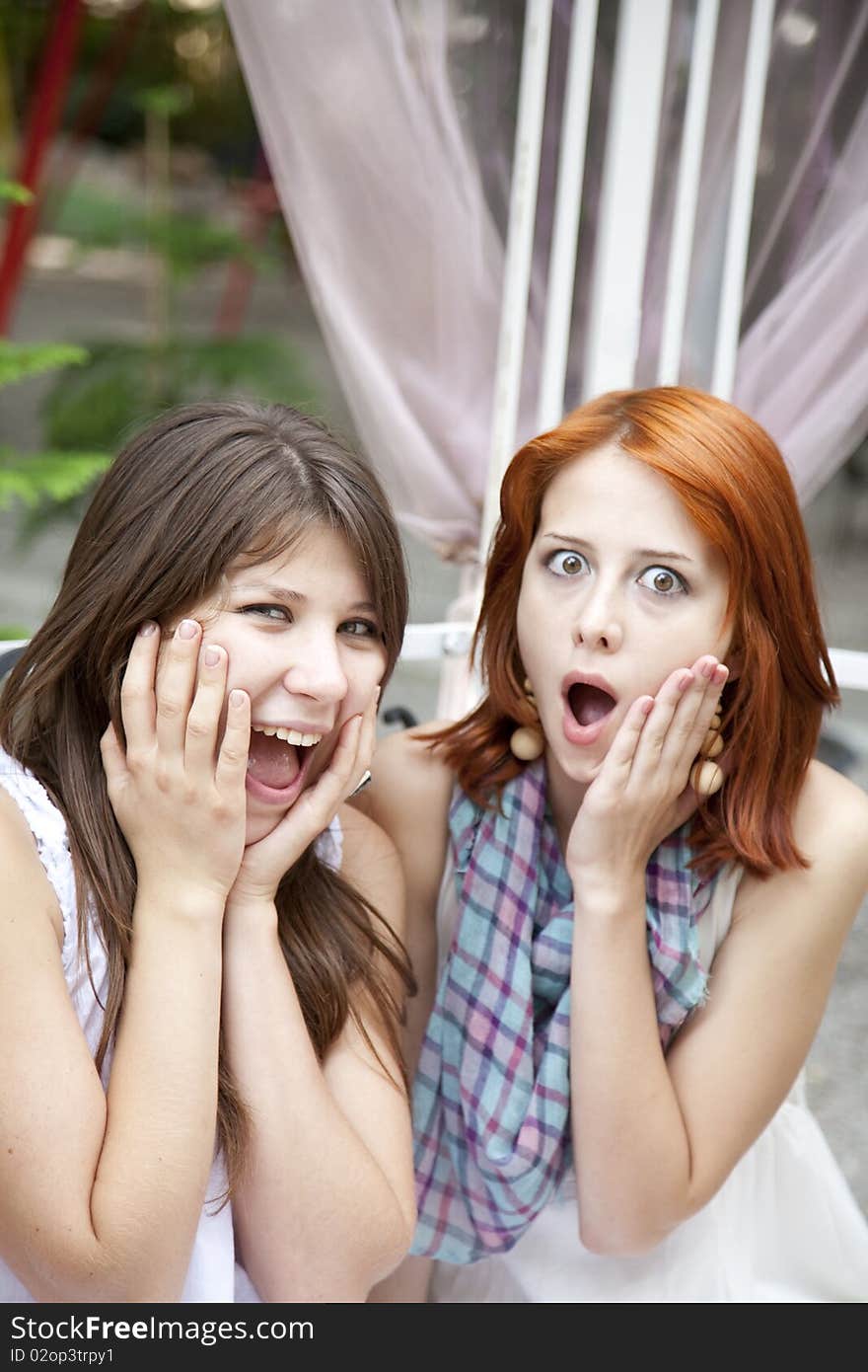 Two girls gossiping on bench at garden.