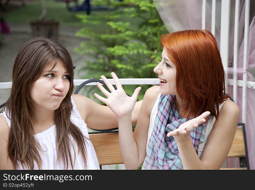 Two girls gossiping on bench at garden.