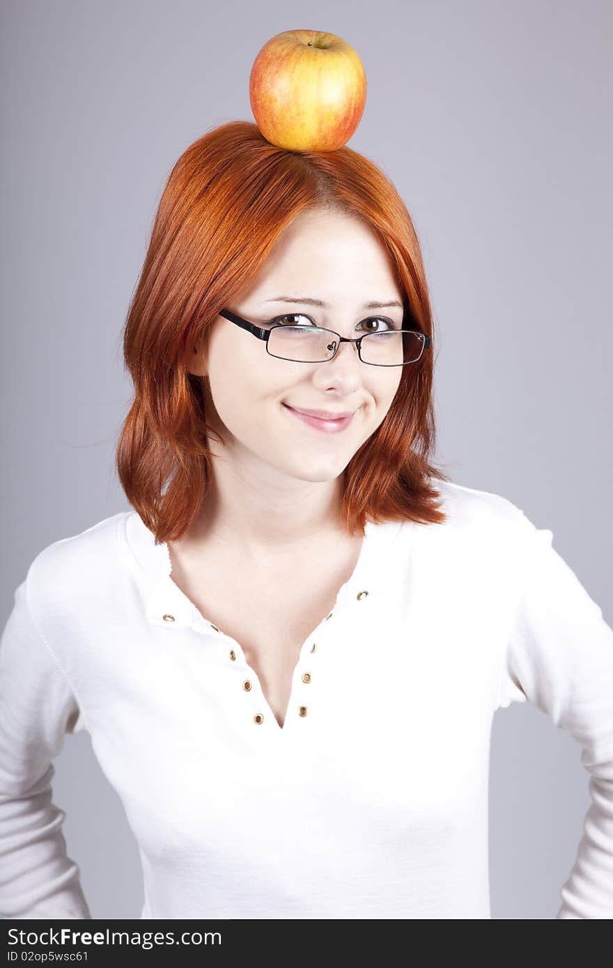 Red-haired girl keep apple on her head. Studio shot.