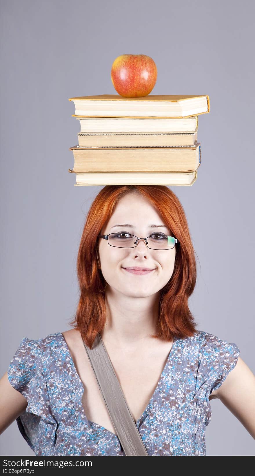 Red-haired girl keep apple and books on her head. Studio shot.