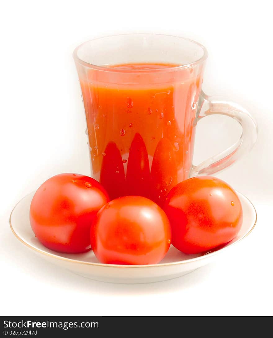 Tomato juice in a clear glass beaker, three ripe red tomatoes on a porcelain dish. Tomato juice in a clear glass beaker, three ripe red tomatoes on a porcelain dish