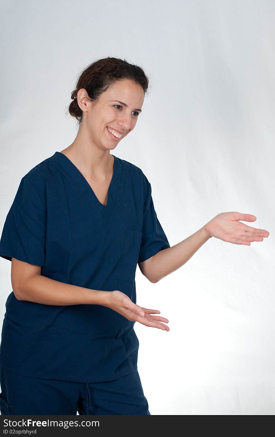 Brunette woman wearing blue scrubs against white background, holding hands out. Brunette woman wearing blue scrubs against white background, holding hands out