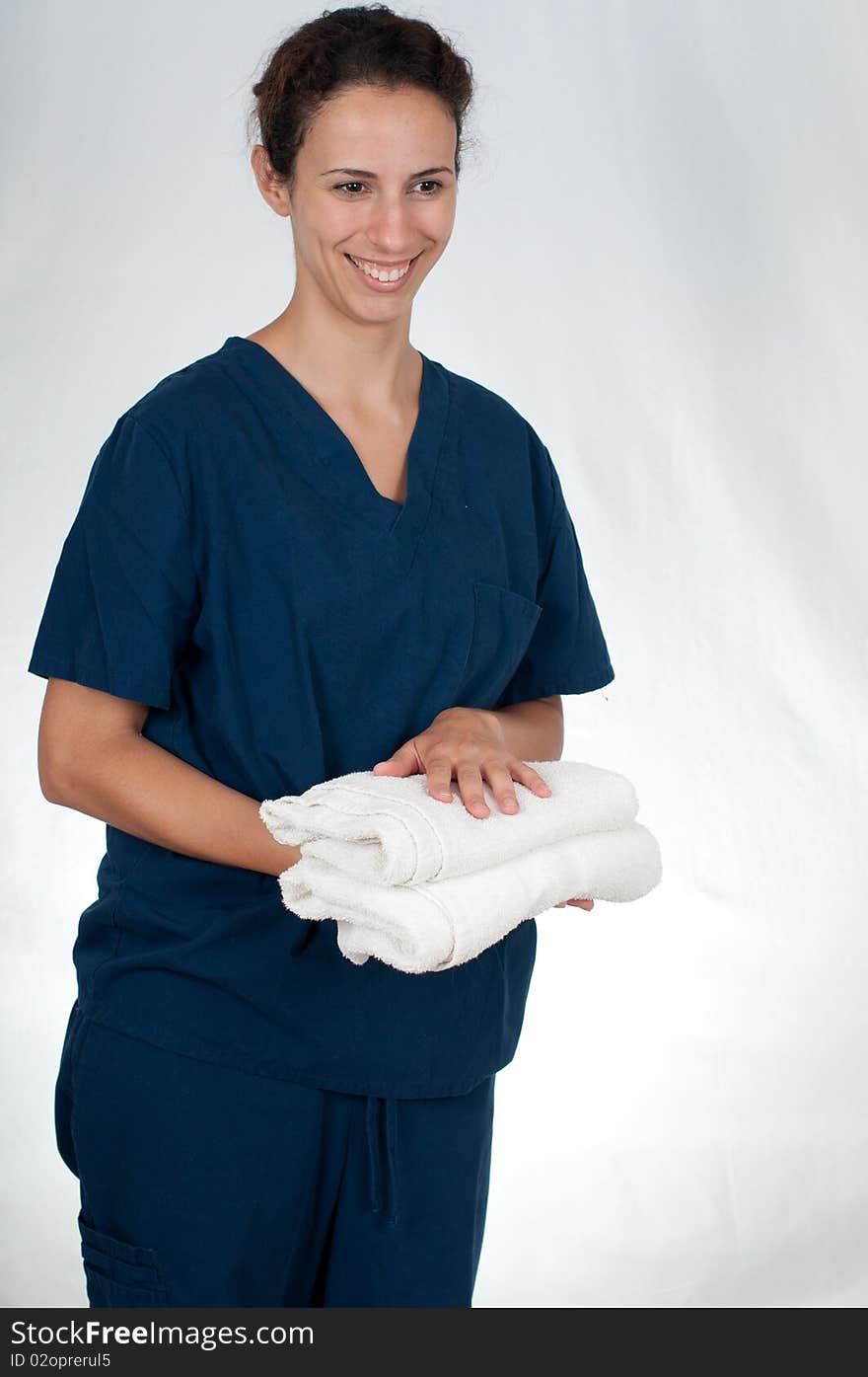 Brunette woman wearing blue scrubs against white background, holding two folded white towels. Brunette woman wearing blue scrubs against white background, holding two folded white towels