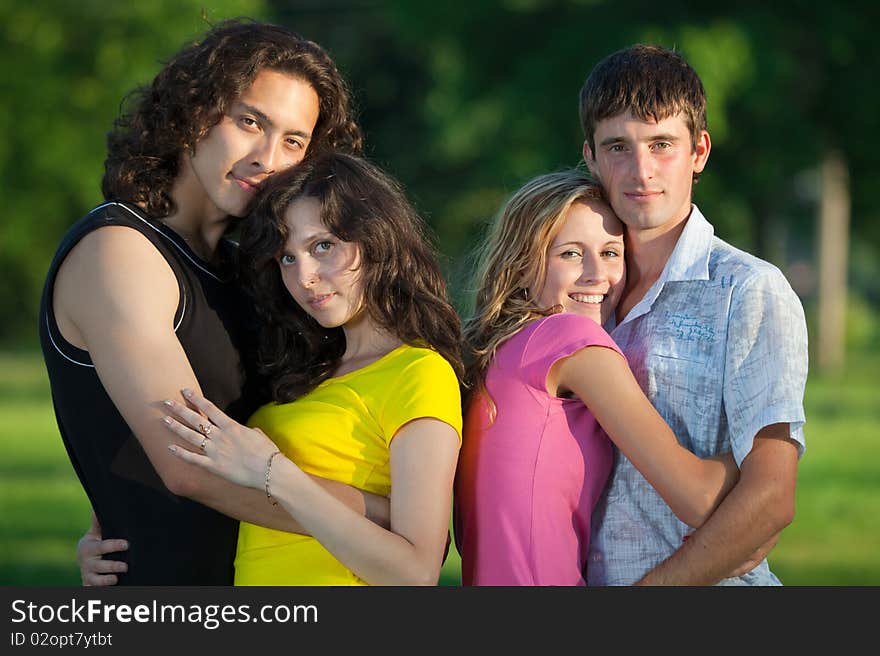 Four young people embrace and stand in the park and look forward