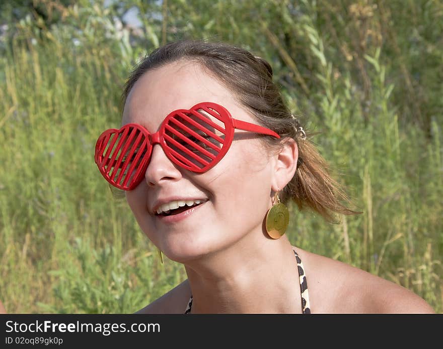 Beautiful young girl smiling in red sunglasses in the form of hearts. Summer portrait, close-up. Outdoor photoset.