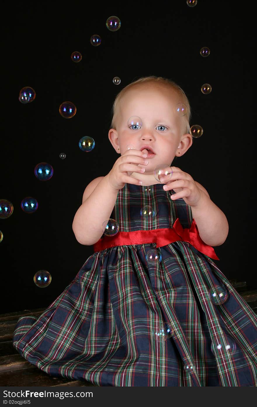 Cute blond toddler girl surrounded by bubbles sitting on a wooden trunk. Cute blond toddler girl surrounded by bubbles sitting on a wooden trunk