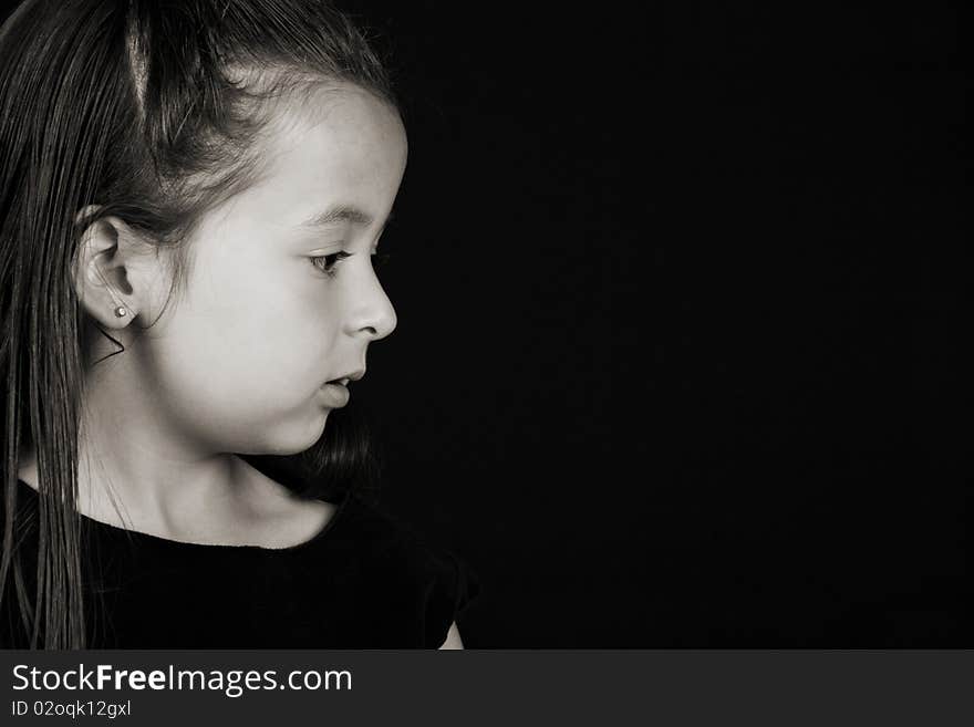 Serious little brunette girl against a black background. Serious little brunette girl against a black background