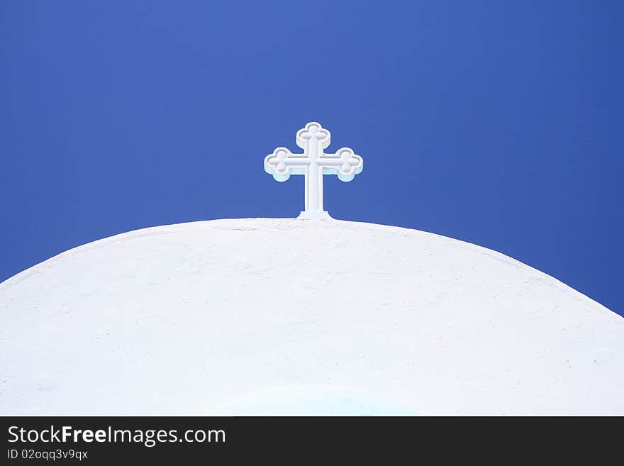 White cross on small greek church under blue sky