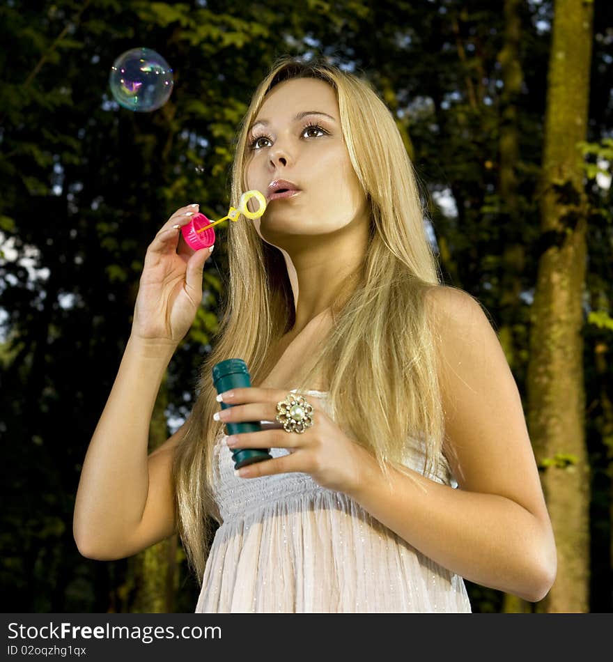 Blonde young woman blowing soap bubbles in summer day. Blonde young woman blowing soap bubbles in summer day