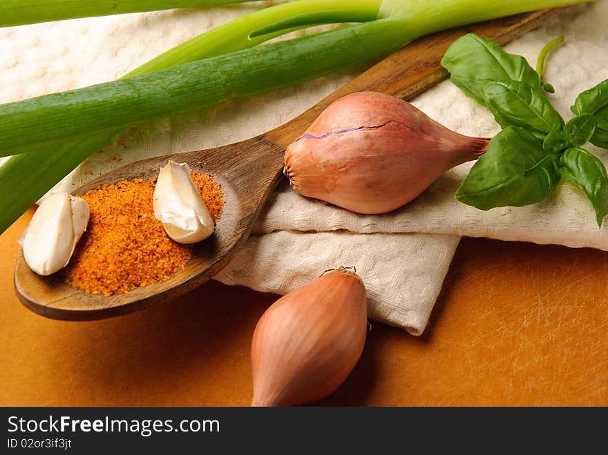 Spices on wooden spoon with green onions and basil leaves on a tea towel. Spices on wooden spoon with green onions and basil leaves on a tea towel