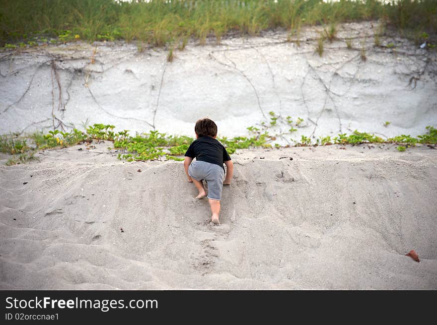 Boy climbing up at the beach. He's about 5 years-old