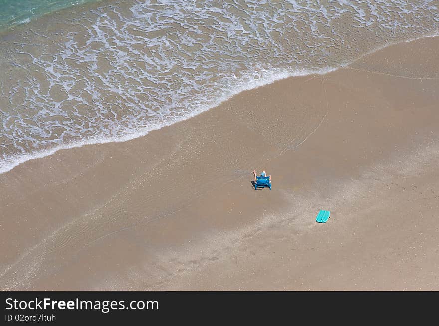 Man alone at the beach on a beach chair. There is a boogie board near him. The ocean is tranquil