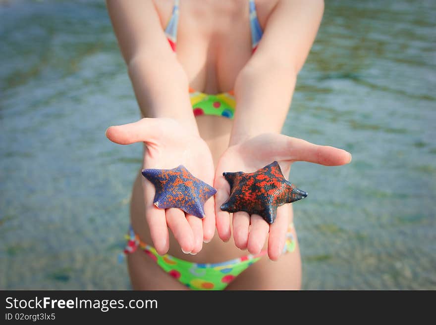 A slender girl in a bikini holding starfish. A slender girl in a bikini holding starfish