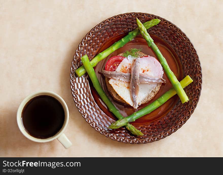 Sandwich with anchovy and tomato on plate, and asparagus and coffee cup on parchment paper