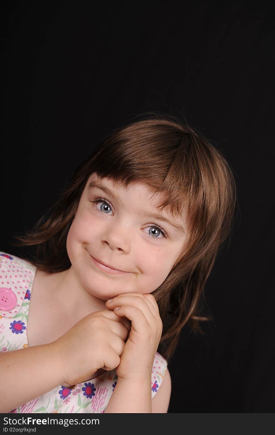 In studio portrait of a young female child, smiling and wearing a floral dress