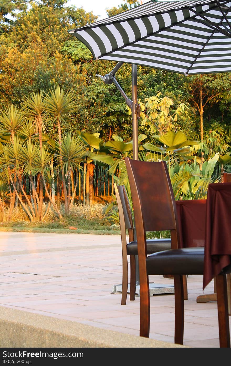 Picture of garden table and chairs with striped umbrella set infront of beautiful natural garden. Picture of garden table and chairs with striped umbrella set infront of beautiful natural garden.