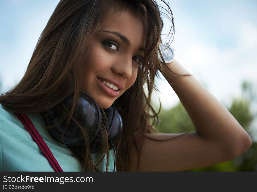 Young beautiful girl with earphones smiling. Outdoor photo.