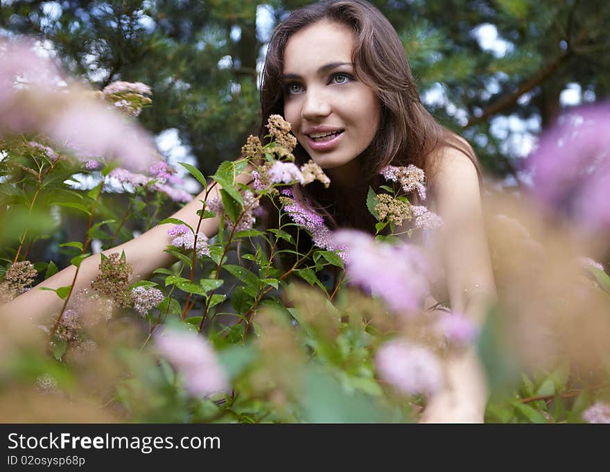 Beautiful girl sitting among the bush flowers