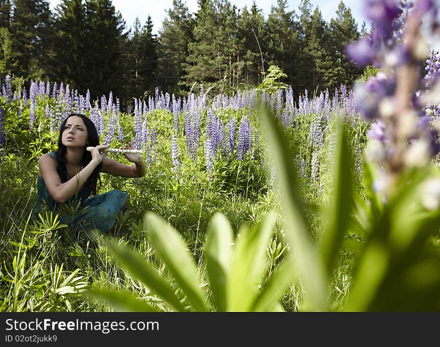 Attractive girl with flute sitting in summer field