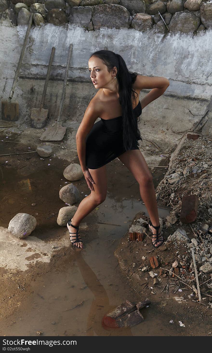 Sexual girl in black dress inside stone quarry among old shovels. Photo.