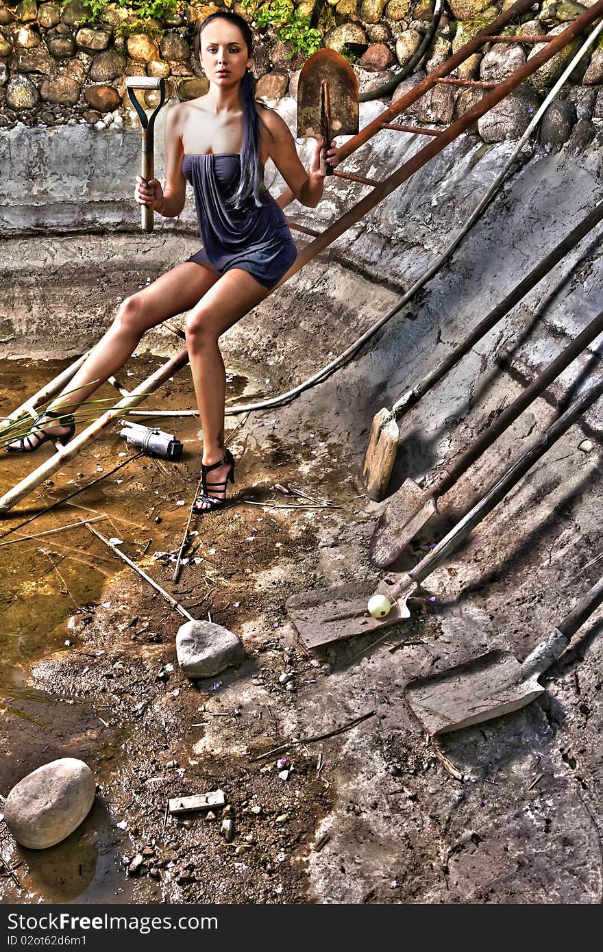 Attractive woman in a stone hole among old shovels. HDR style Photo.