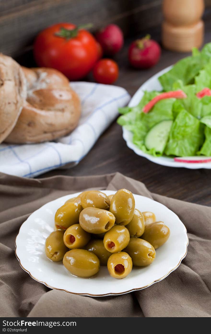 Close up of green olives in small plate with some other food on the background. Close up of green olives in small plate with some other food on the background