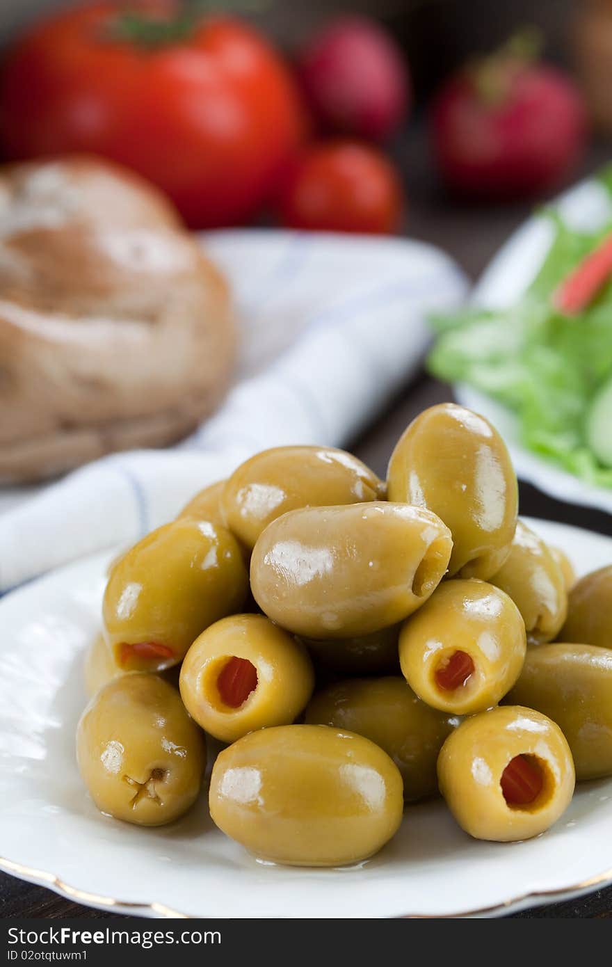 Close up of green olives in small plate with some other food on the background