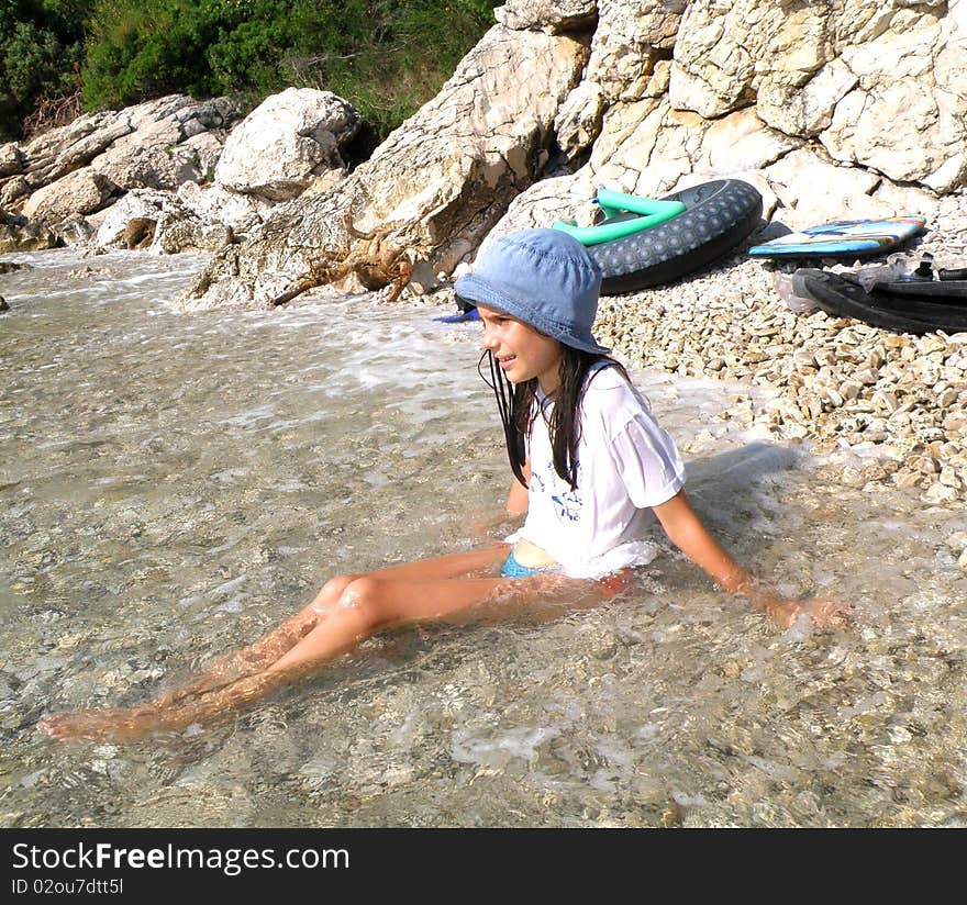 Girl with cap and white shirt sitting in shallow water. Girl with cap and white shirt sitting in shallow water