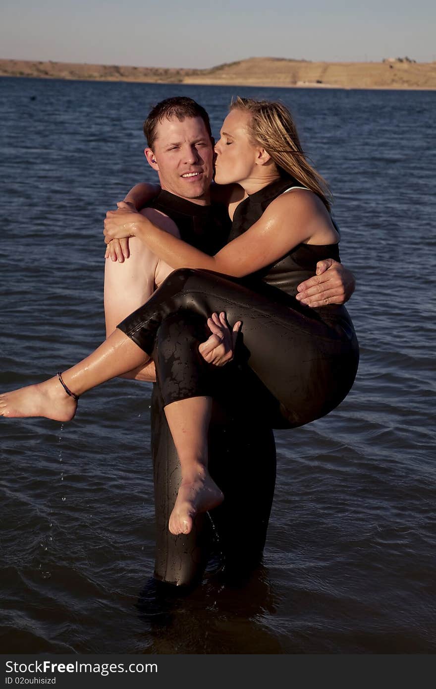 A couple together in their wet suits, showing their love by him holding her in his arms while she kisses him on the cheek. A couple together in their wet suits, showing their love by him holding her in his arms while she kisses him on the cheek.