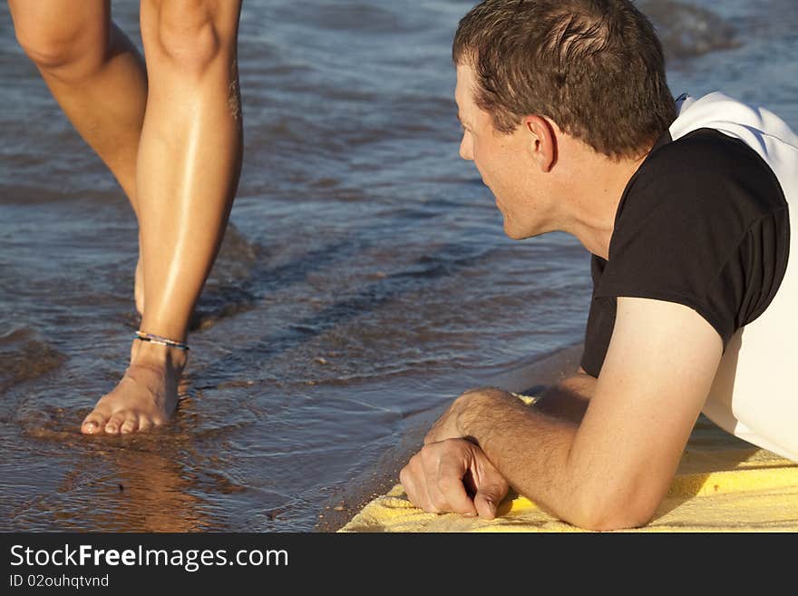 A man laying on a yellow towel, watching the legs of a woman walking by. A man laying on a yellow towel, watching the legs of a woman walking by.