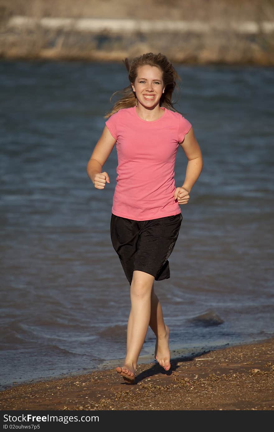 A young teenager in a pink shirt and black shorts running barefoot on the beach. A young teenager in a pink shirt and black shorts running barefoot on the beach.