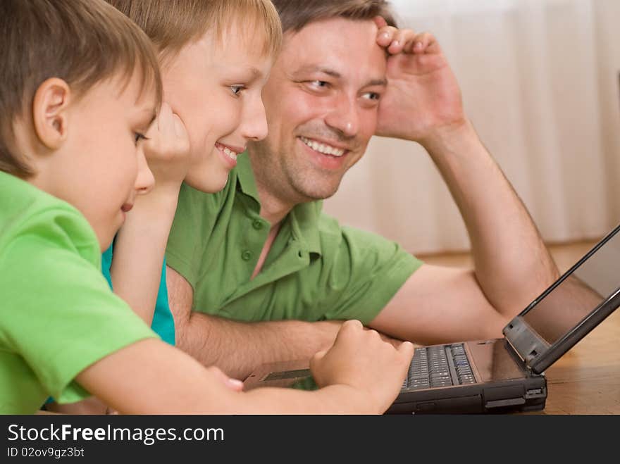 Father with his sons is on the carpet with laptop