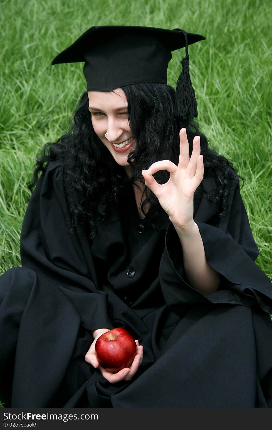 Young smiling caucasian student with okay sitting on the green grass