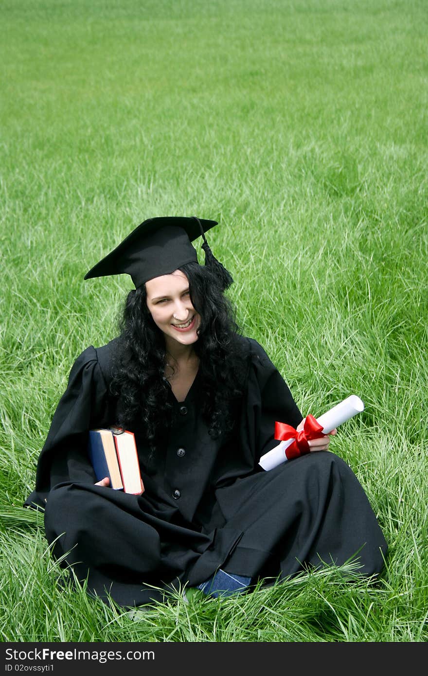 Happy bachelor with diploma sitting on the grass