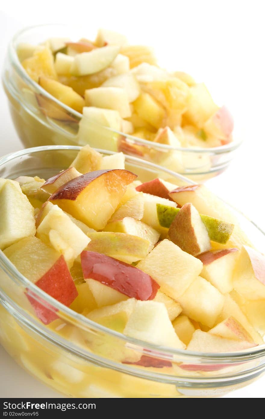 Fruit salad with apples, oranges, peaches, pears and orange juice. Decomposed in two glass plates. Isolated on white background