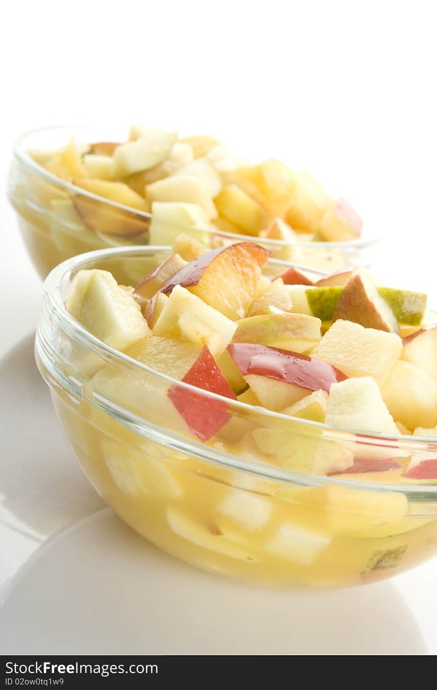 Fruit salad with apples, oranges, peaches, pears and orange juice. Decomposed in two glass plates. Isolated on white background