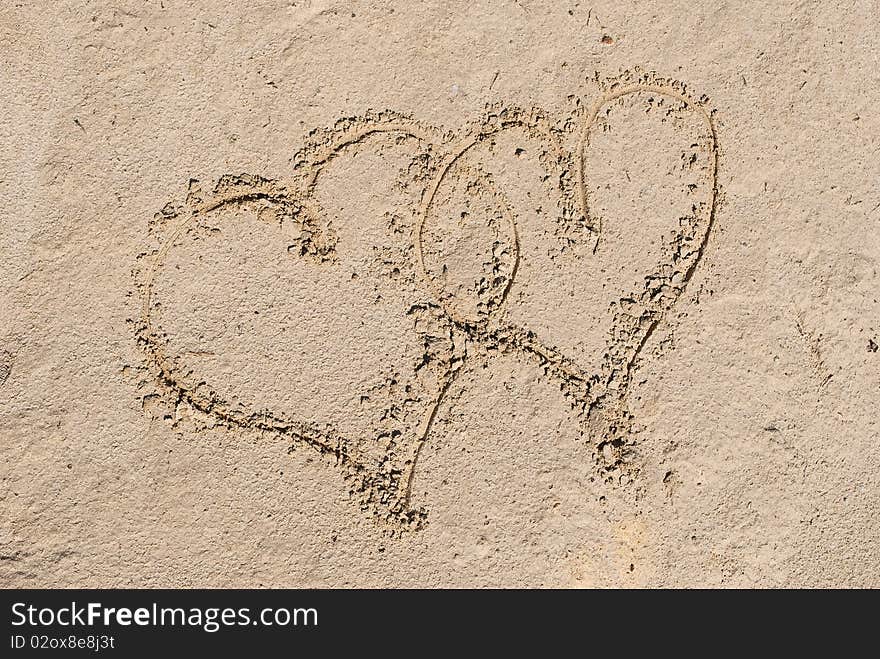 Two entangled hearts drawn out on a sandy beach