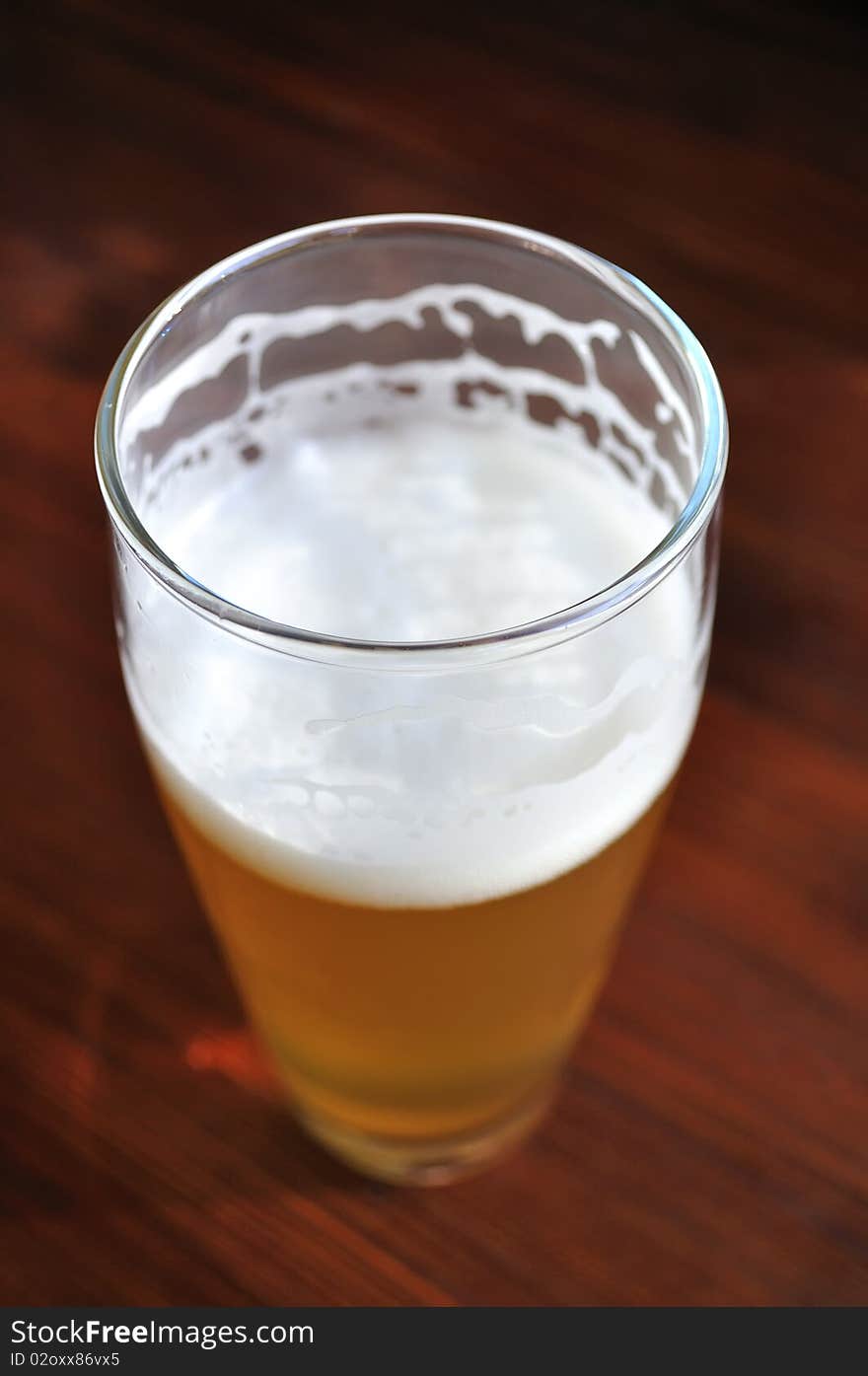 An unfinished glass of unfiltered beer on a wooden table. An unfinished glass of unfiltered beer on a wooden table