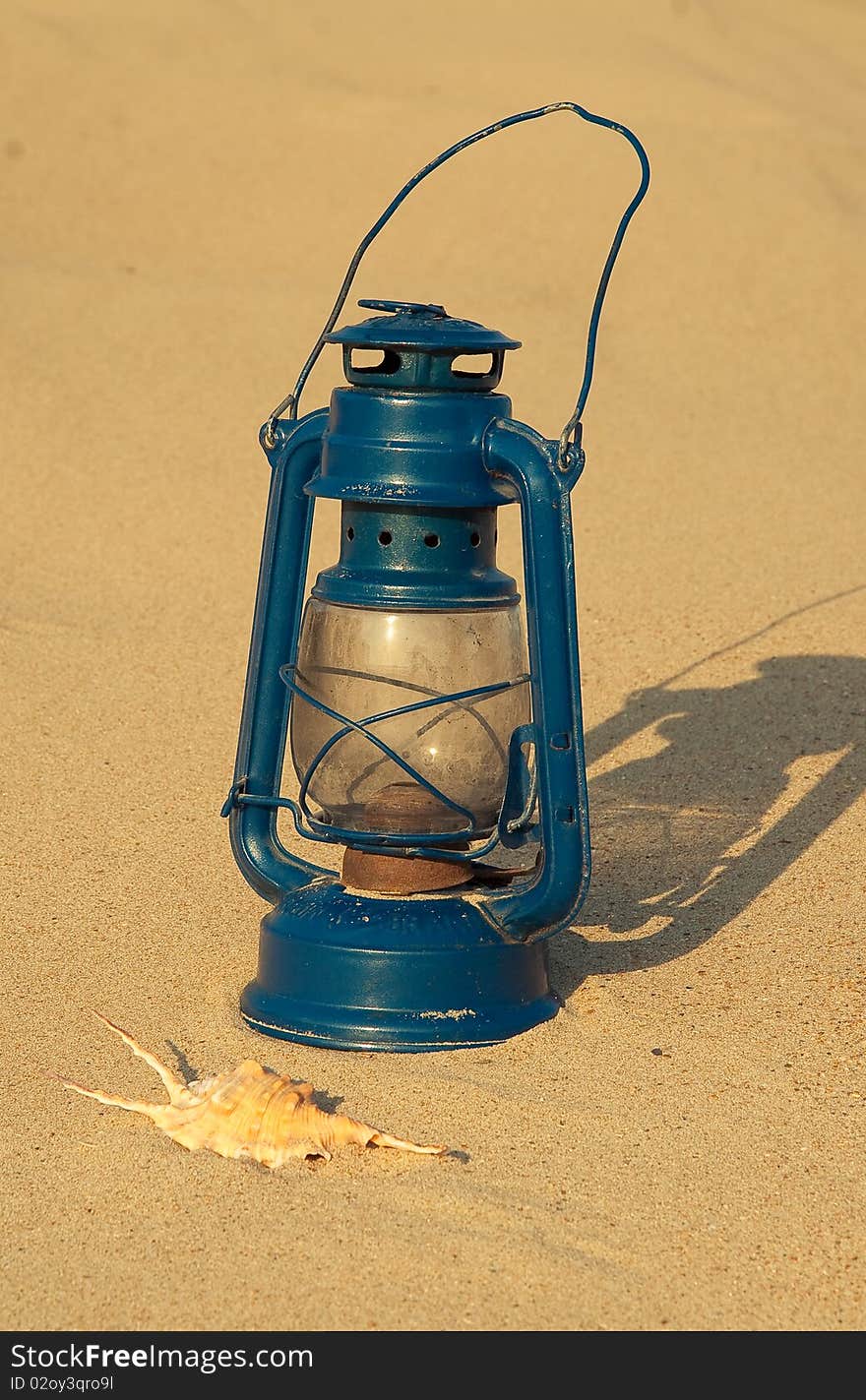 Vintage blue gasoline lantern and sea shell on the sand background. Vintage blue gasoline lantern and sea shell on the sand background